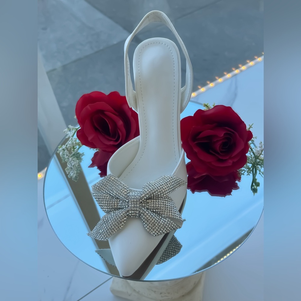 White pointed toe heels with rhinestone bow
